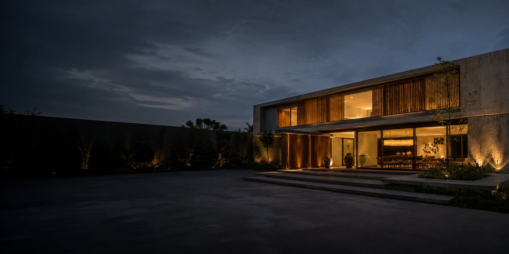 Residência contemporânea em concreto e madeira, iluminada ao anoitecer